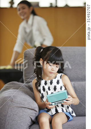 a little girl is holding a handheld video game when mom looks at her. 31492707