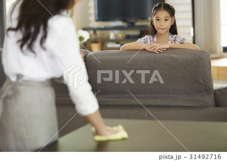 A little girl is sitting on the sofa and watching mothe cleaning. 31492716