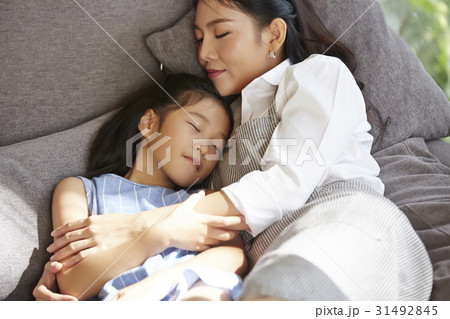Mother and little girl are embracing and sleeping on sofa. 31492845