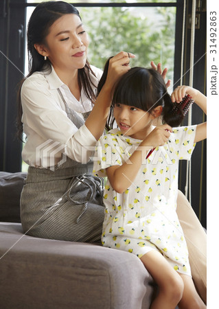 The mother is smiling when tying her daughter's hair 31492863