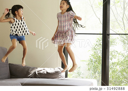 Two Asian girls are jumping on a sofa in living room. 31492888