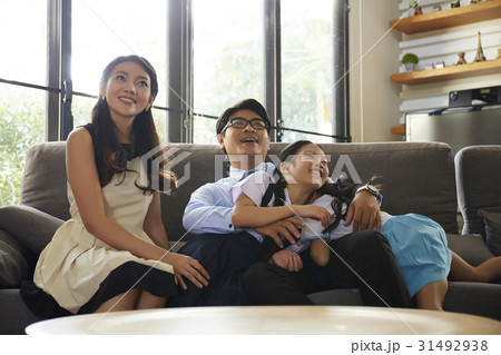A happy family of parents and two girls is sitting on sofa and looking at something. 31492938