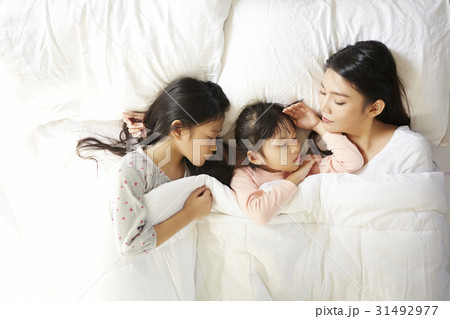 mom and two kids are sleeping on the bed. 31492977