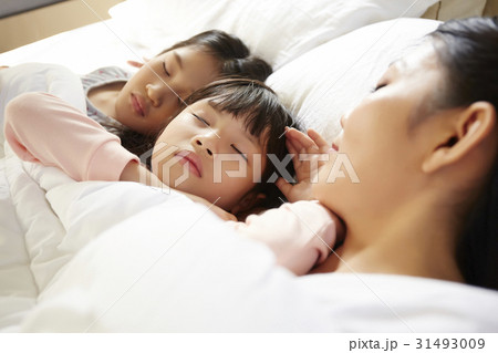 mother and two kids are taking a nap on the bed . 31493009