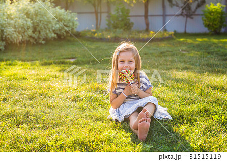 cute little girl eating a lollipop on the grass in cute little girl eating a lollipop on the grass in 31515119