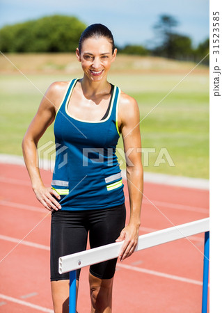 Portrait of female athlete standing beside hurdle 31523585