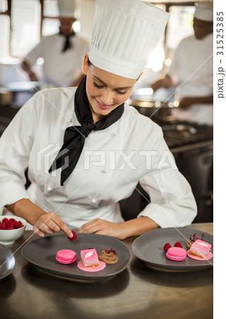 Smiling female chef finishing dessert plates Smiling female chef finishing dessert plates 31525385