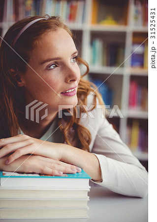 Thoughtful school teacher with books in library Thoughtful school teacher with books in library 31525431