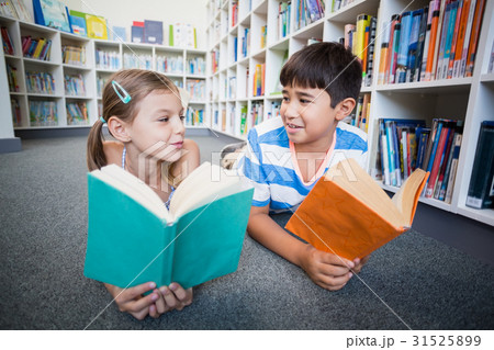 School kids lying on floor and reading a book in library School kids lying on floor and reading a book in library 31525899