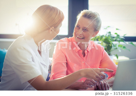 Female nurse and senior woman smiling while using laptop 31526336