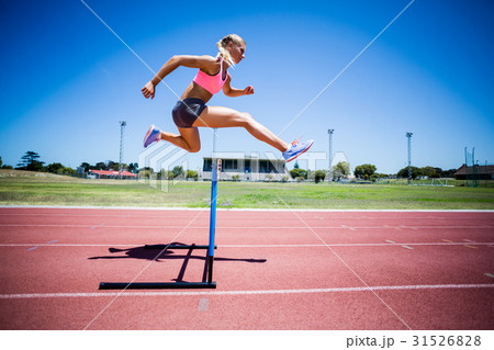 Female athlete jumping above the hurdle 31526828