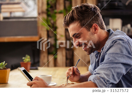 Profile view of hipster man using tablet at cafe 31527572