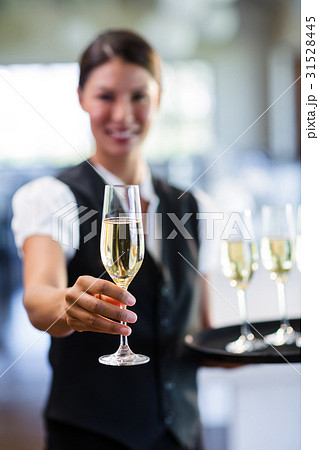 Portrait of smiling waitress offering a glass of champagne Portrait of smiling waitress offering a glass of champagne 31528445