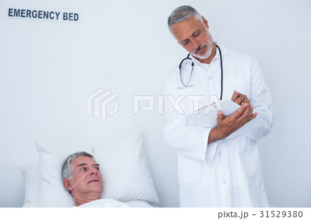 Male doctor writing medical report of senior man on clipboard Male doctor writing medical report of senior man on clipboard 31529380