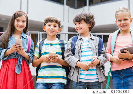 Kids holding mobile phone and digital tablet standing on school terrace 31556395