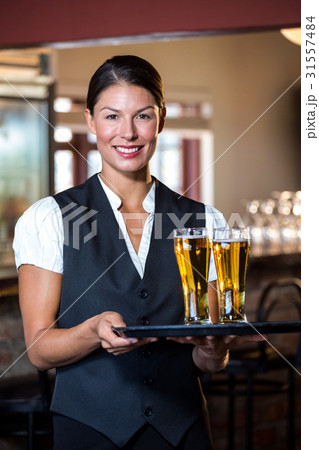 Portrait of waitress holding serving tray with two glass of beer Portrait of waitress holding serving tray with two glass of beer 31557484