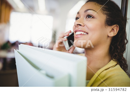 Close-up of businesswoman holding files while using mobile phone in cafeteria 31594782