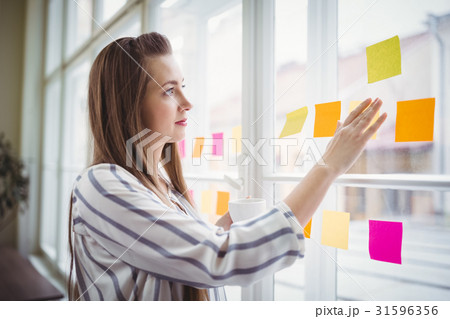 Young businesswoman looking at adhesive notes on window in creative office Young businesswoman looking at adhesive notes on window in creative office 31596356