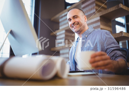 Happy businessman holding cup at computer desk 31596486
