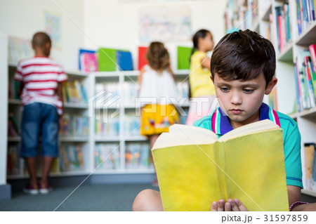Elementary boy reading book at school library Elementary boy reading book at school library 31597859