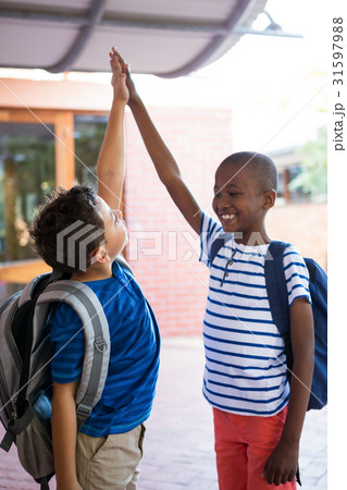 Playful classmates giving high-five at corridor Playful classmates giving high-five at corridor 31597988
