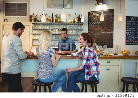 Waiter looking at female customers sitting at counter in cafe 31599175