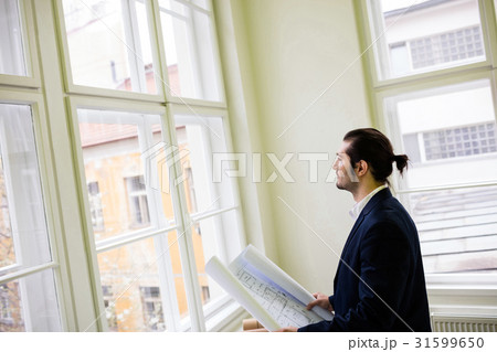 Interior designer holding blueprint while looking through window 31599650