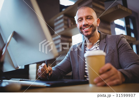 Creative businessman holding disposable cup while using graphics tablet 31599937