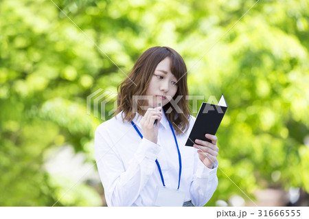 手帳を見て悩む女性 白シャツ ネームプレート 手帳を見て悩む女性 白シャツ ネームプレート 31666555
