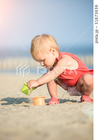 Baby girl in red dress playing on sandy beach near 31673636