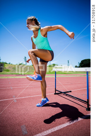 Female athlete jumping above the hurdle Female athlete jumping above the hurdle 31708918