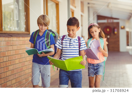 School kids reading books while walking in corridor 31708924