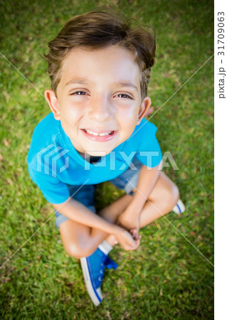 Young boy sitting on grass and smiling at camera in park Young boy sitting on grass and smiling at camera in park 31709063