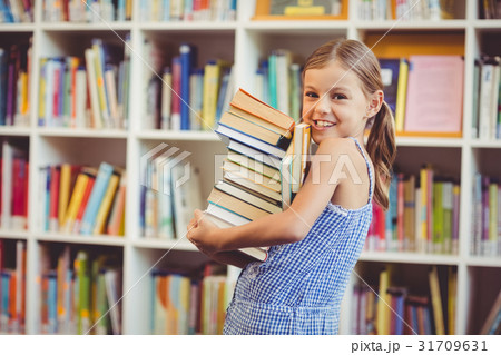 School girl holding stack of books in library 31709631