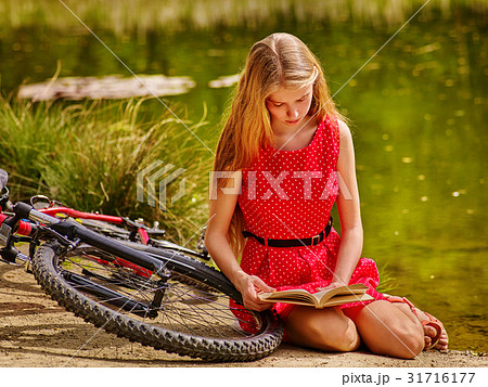 Girl in cycling reading book near bicycle into 31716177