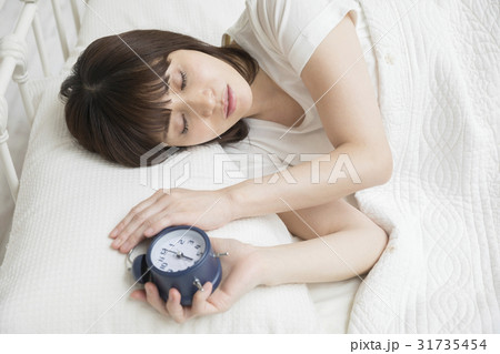 目覚まし時計を持ったまま寝る女性　二度寝イメージ 31735454