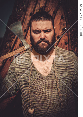 Viking with axe standing near drakkar on the Viking with axe standing near drakkar on the 31759539
