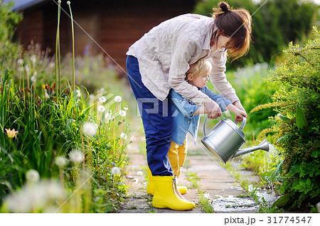 Cute toddler boy and his young mother watering plants in the garden Cute toddler boy and his young mother watering plants in the garden 31774547
