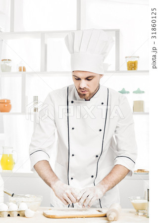 Chef man in uniform kneading raw dough in kitchen Chef man in uniform kneading raw dough in kitchen 31860125