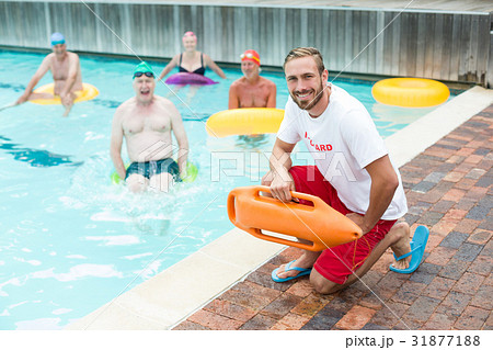 Male lifeguard crouching while swimmers swimming in pool 31877188