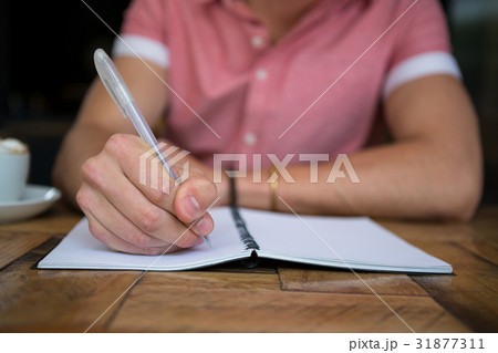Man writing in diary at table in coffee shop Man writing in diary at table in coffee shop 31877311