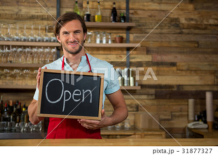 Happy barista holding open signboard in coffee shop Happy barista holding open signboard in coffee shop 31877327