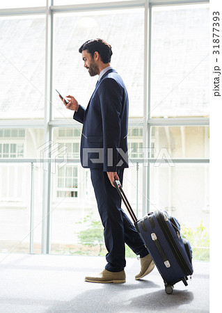 Businessman with trolley bag using mobile phone Businessman with trolley bag using mobile phone 31877393