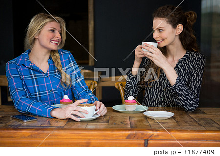 Smiling female friends having coffee while talking in cafeteria Smiling female friends having coffee while talking in cafeteria 31877409