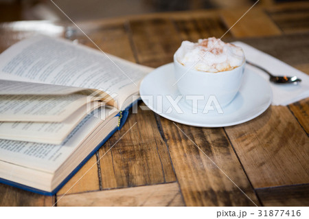 Coffee cup by open book on table in cafeteria Coffee cup by open book on table in cafeteria 31877416