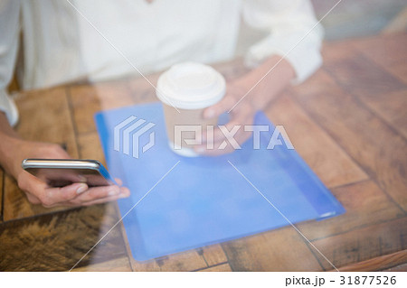 Woman holding coffee cup and mobile phone seen through cafe window 31877526