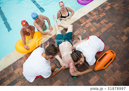 Friends looking at lifeguards saving unconscious senior man at poolside 31878997