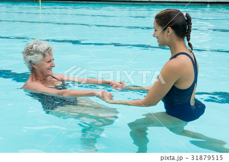 Female coach helping senior woman in swimming pool 31879515
