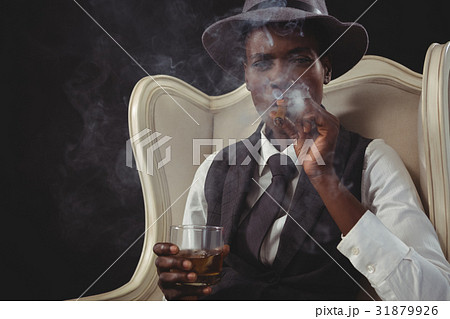 Androgynous man smoking cigar while while sitting on a chair Androgynous man smoking cigar while while sitting on a chair 31879926