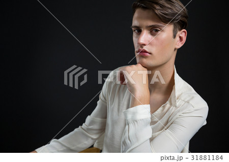Androgynous man sitting on chair with hand on his chin 31881184